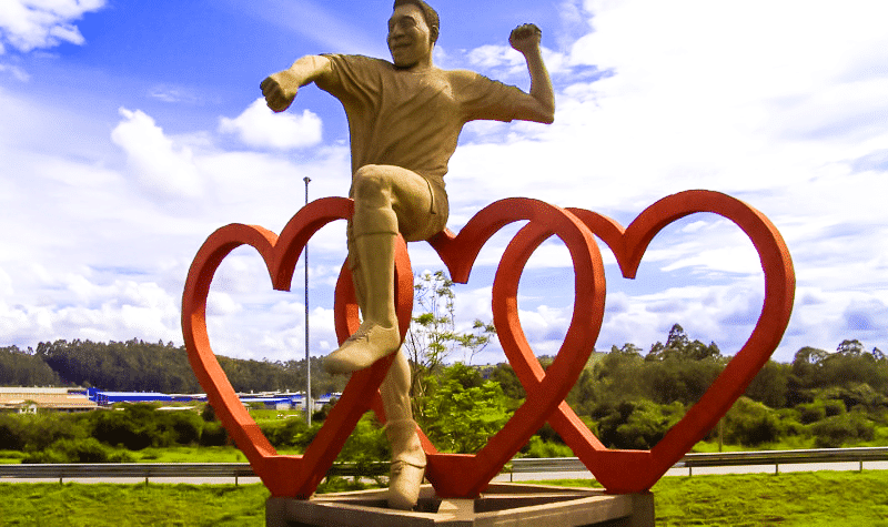 Estátua do jogador Pelé em sua famosa comemoração com soco no ar, posicionada acima de três grandes corações vermelhos entrelaçados, localizada na entrada da cidade de Três Corações, Minas Gerais.