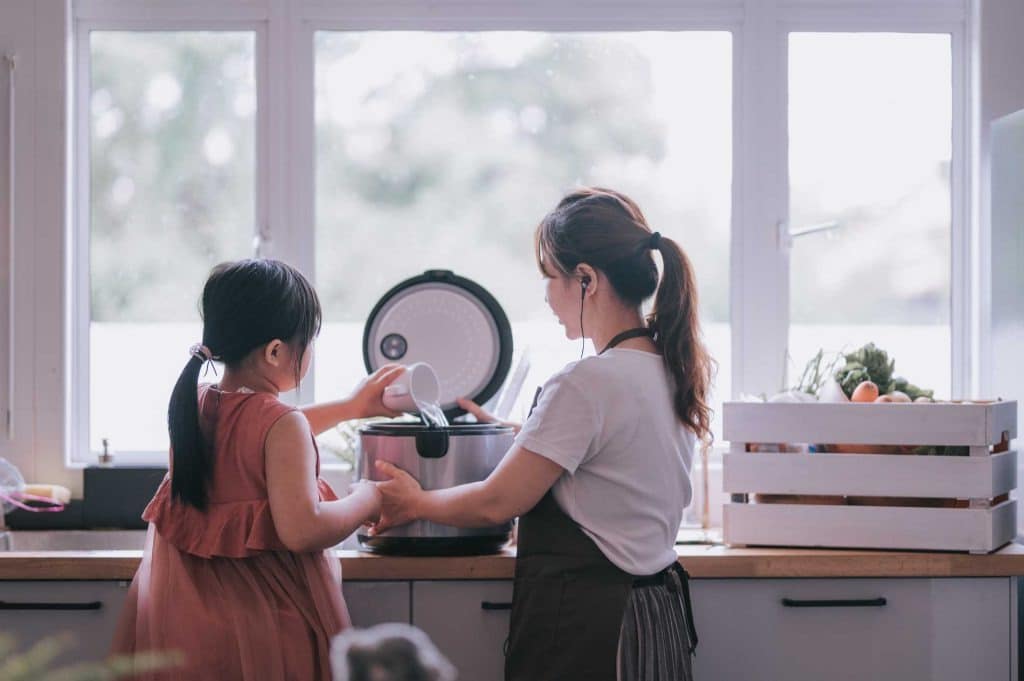 Mãe e filha preparando receitas na panela de arroz juntas na cozinha.