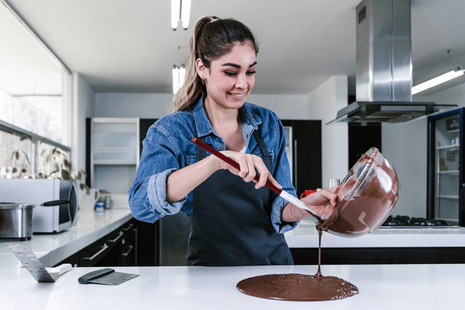 Mulher sorrindo enquanto tempera chocolate na bancada para aprender como fazer ovo de Páscoa em casa.