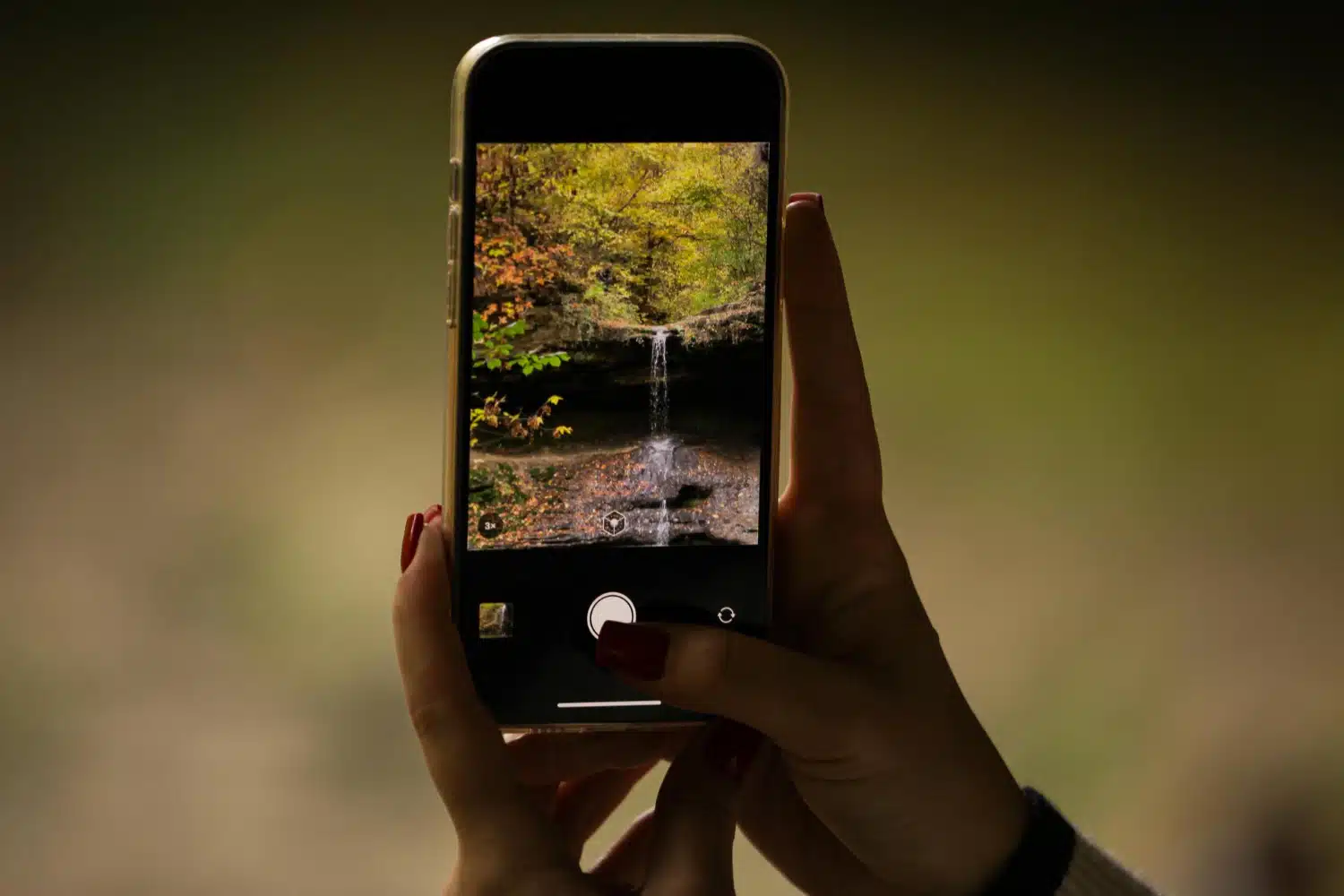 Mão feminina usando iPhone Pro para fotografar cachoeira na floresta com zoom de 3x.