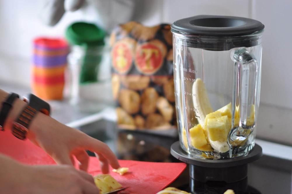 Mãos cortando abacaxi para colocar no liquidificador com banana, preparando a base de receitas fit práticas e saudáveis na cozinha.