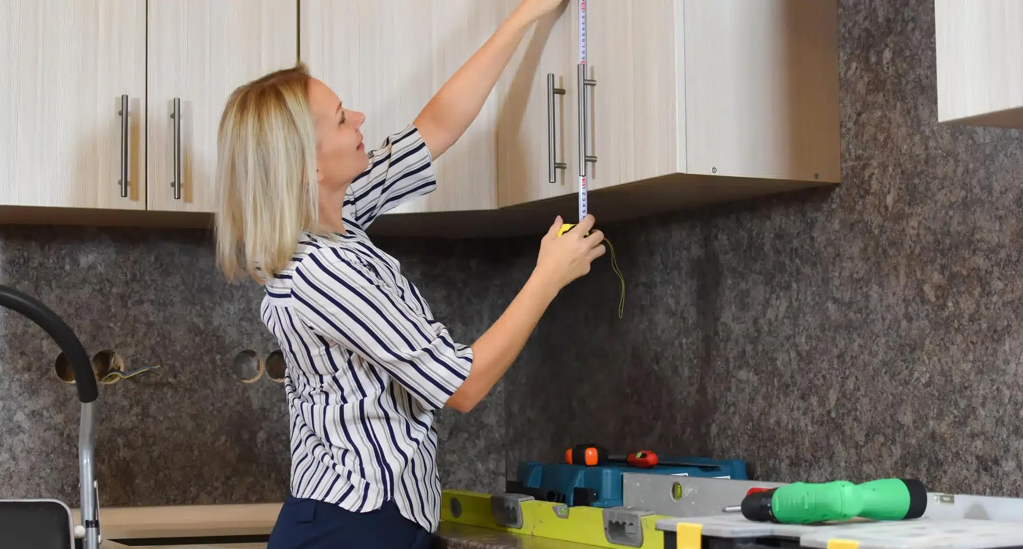 Mulher medindo armário de cozinha com trena em cozinha planejada.